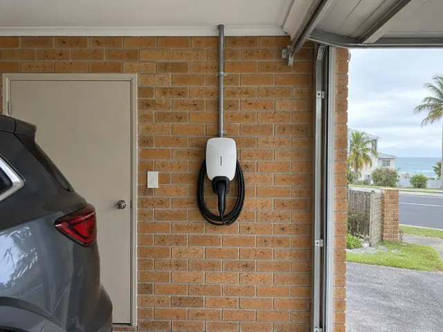 Wall-mounted EV charger on a brick garage wall beside a car and roller door in Coolangatta